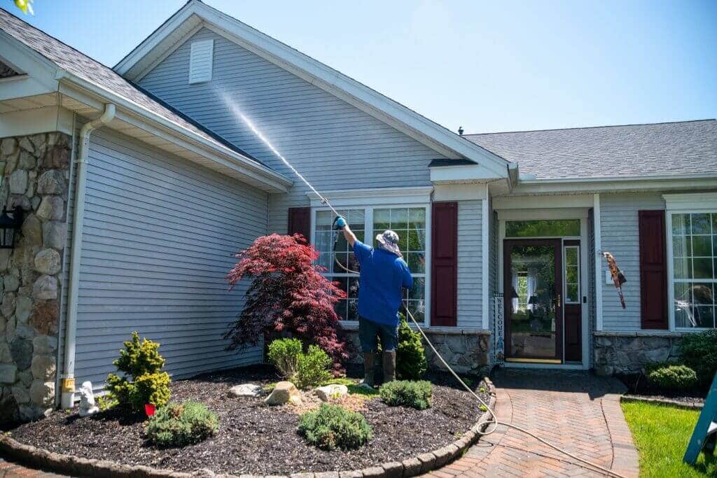 A professional cleaner in a blue shirt and hat, using a long wand to pressure wash